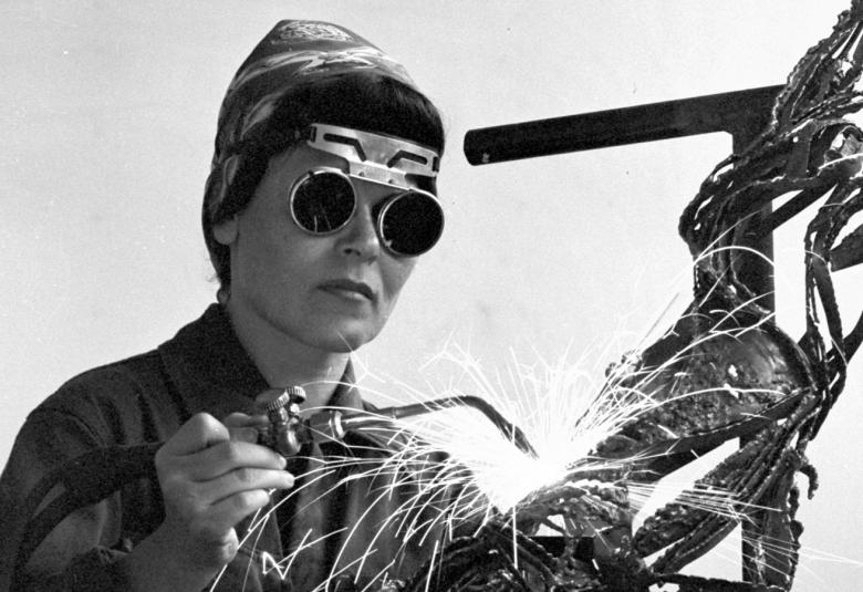 Kuvassa on Eila Hiltunen hitsauskypärä päässään hitsaamassa metallia.