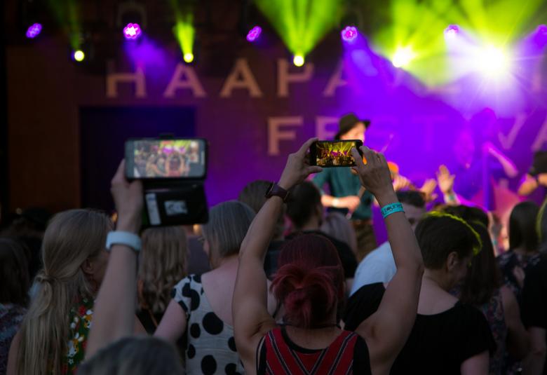 Kuvassa on hämärää sekä violettisävyä ja yleisöä takaapäin sekä valaistusta lavalta.