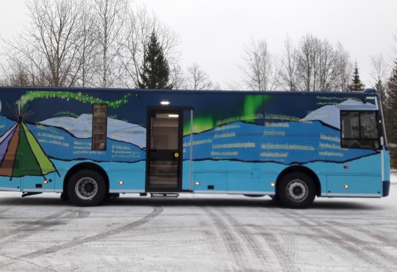 Kuvassa on Inarin kirjastoauto, joka on sinisävyinen ja siinä on lappi-aiheisia kuvia sekä tekstiä.