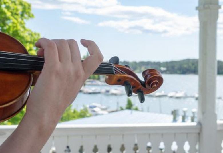 Kuvassa näkyy viulu ja soittajan käsi ja taustalla kesäistä Naantalia.