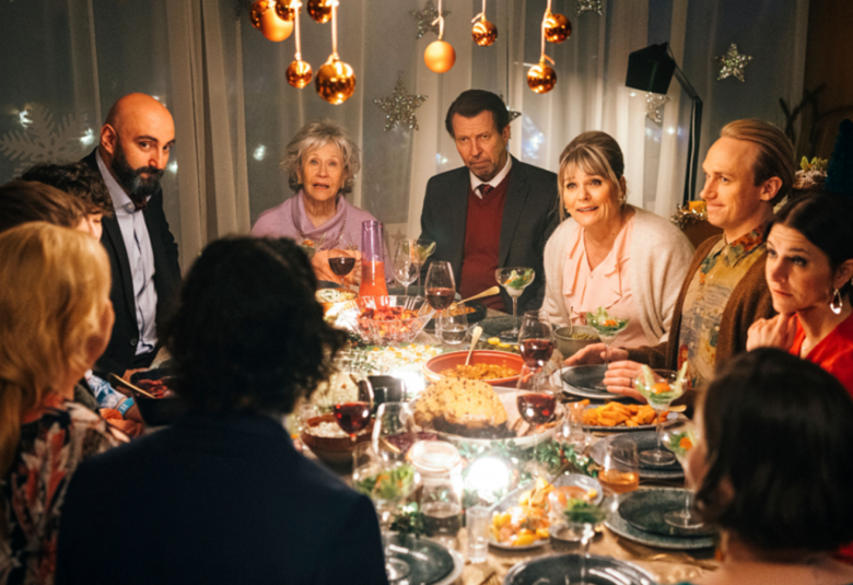 Kuvassa ovat elokuvan näyttelijät joulupöydän ympärillä keskustelemassa iloisesti ja pöydässä on ruokaa. 