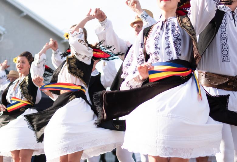 Kuvassa on tanssijoita tanssimassa vauhdikkaasti valkoisissa mekoissa, joissa on vihreän punainen vyö.