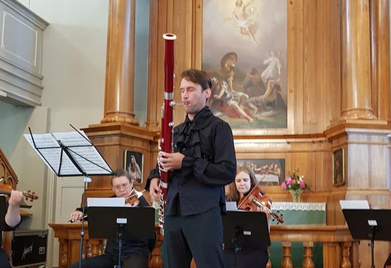 Kuvassa on Bence Boganyi soittamassa fagottia ja viulistit ja basson soittaja taustalla.