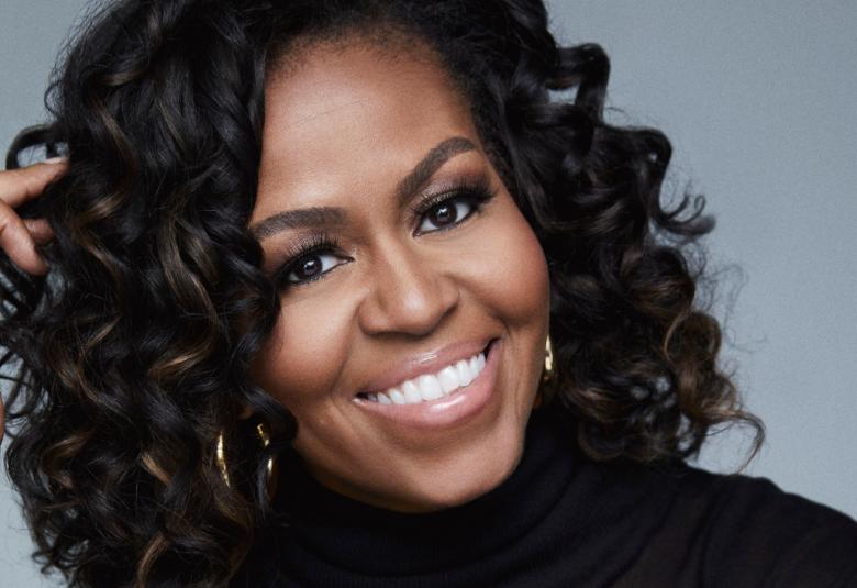 Kuvassa on Michelle Obaman kasvokuva ja hänellä on pitkät kiharat hiukset.  Kuvassa hän nojaa oikeaan käteensä.