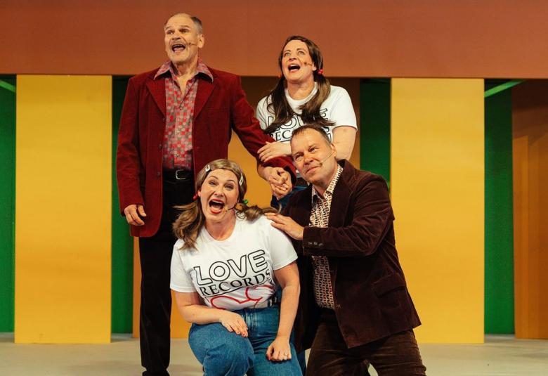 Kuvassa on neljä näyttelijää, joista kaksi on puolikyykyssä lattialla ja kaksi muuta seisomassa.