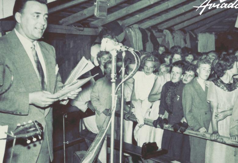 Osa kirjan kannesta. Kuvassa on Olavi Virta laulamassa yleisölle, jota näkyy hänen ympärillään aidan takana.  Kuva on musta-valkoinen.