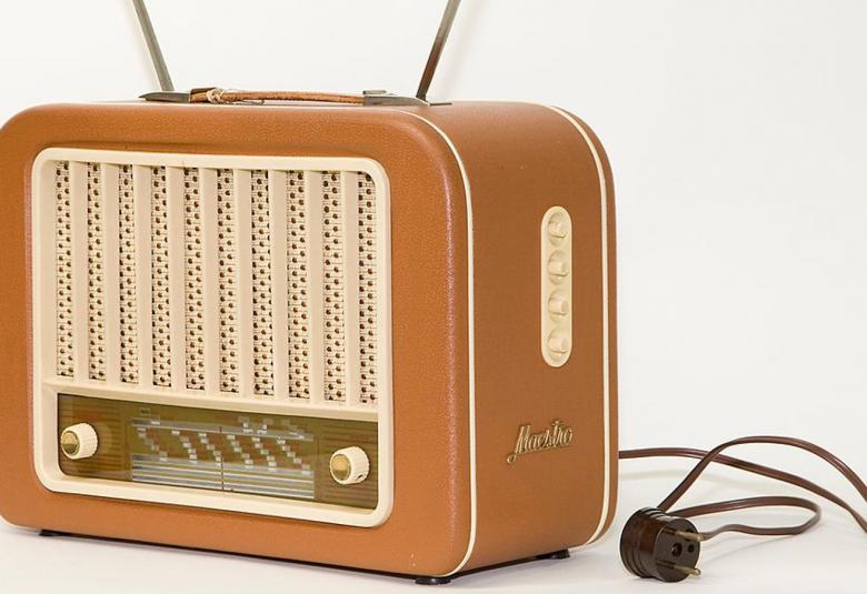 Kuvassa on vanhanaikainen hiukan kulmikas vaalean ruskea radio ja sen töpseli on irrallaan vieressä.