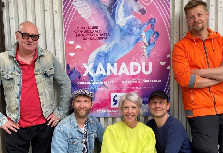 Xanadun suunnittelijat Jyri Numminen (vas.), Juho Lindström seisomassa ja Pauliina Salonius, Timjami Varamäki ja Pekka Siistonen kyykyssä alhaalla.  Taustalla näkyy Xanadun juliste.