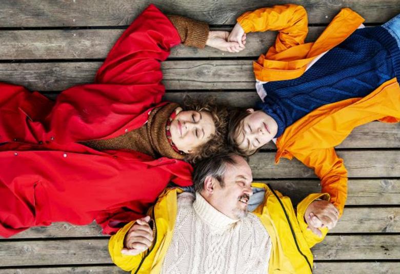 Kuvassa ovat ylhäältä päin kuvattuna punaisessa takissa Heidi Herala, keltaisessa takissa ja valkoisessa villapaidassa Juhani Laitala ja punaisessa takissa ja tumman sinisessä puserossa tytärtä esittävä näyttelijä. He makaavat lattialla.  