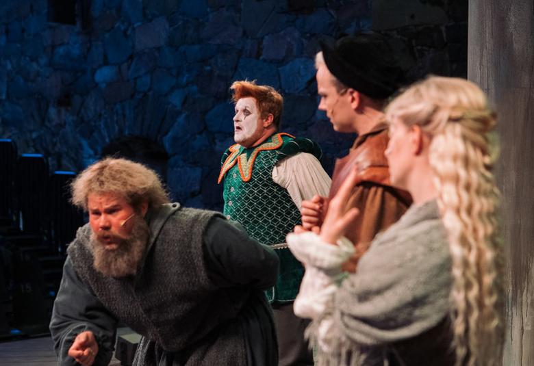 Keskellä parrakas mies on kumartuneena ja takana on vasemmalla mies maalatuissa kasvoissa, mies mustassa baskerissa ja nainen vaaleissa pitkissä hiuksessa.