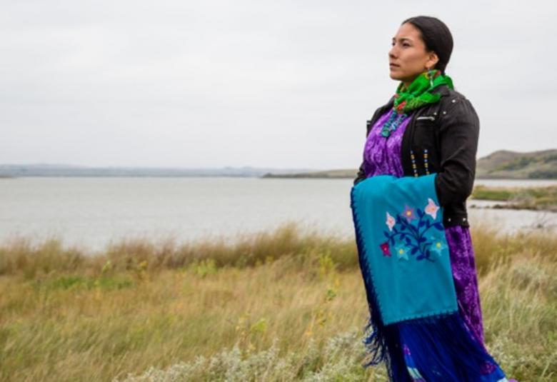 Kuvassa on Floris Ptesáŋ Huŋká seisomassa sivuttain aukeassa maisemassa, jossa on peltoa ja harmaa taivasa.