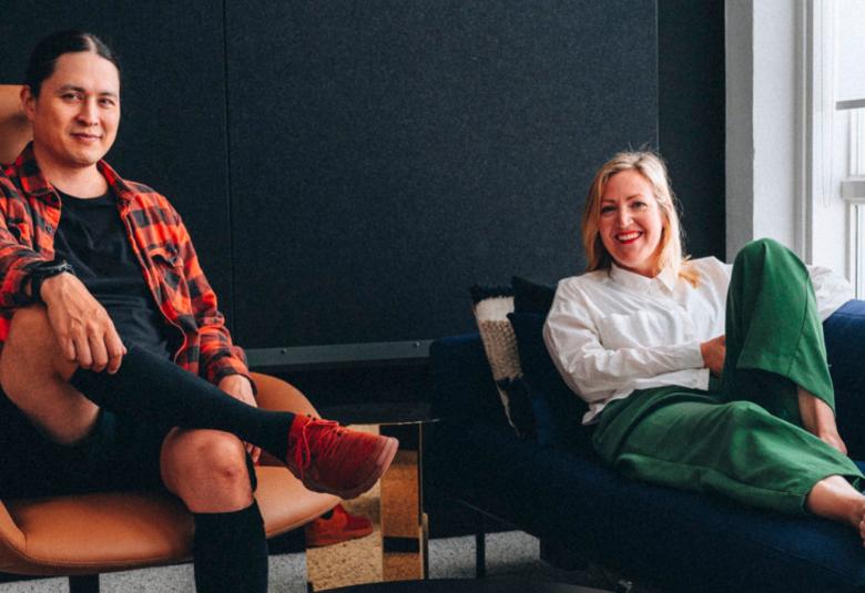 Kuvassa ovat Yuki Abe ja Anna Salonen löhöämässä sohvilla ja taustalla on tummaa seinää.