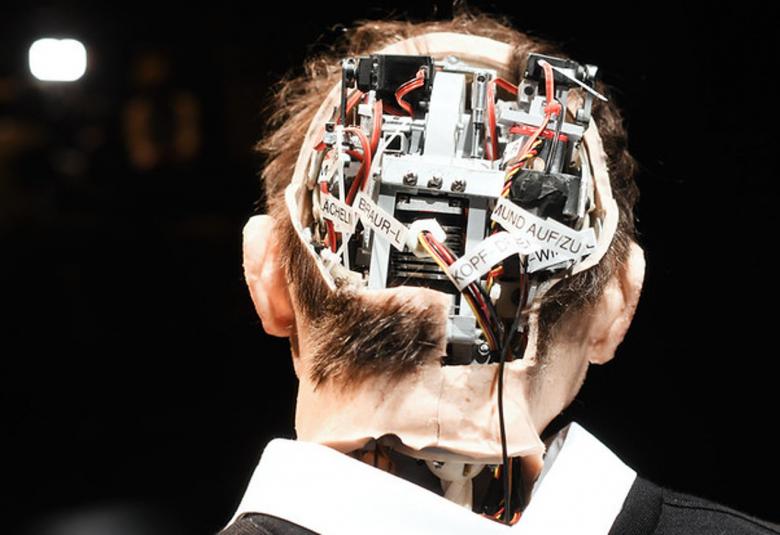 Kuvassa on miehen takaraivo, jossa on aivojen kohdalla tietokoneen koneistoa.