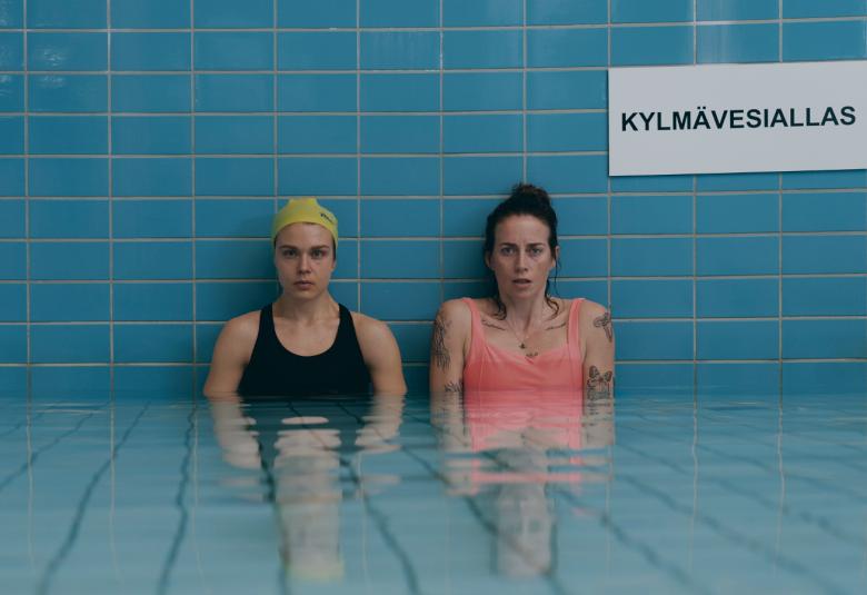 Kuvassa ovat seisomassa Alina Tomnikov ja Iina Kuustonen turkoosissa vesialtaassa vyötäröä myöten. Seinällä on kyltti kylmävesiallas.