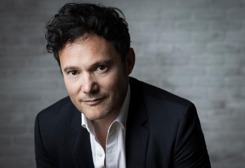 Kuvassa on Matthew Halls puolivartalokuvassa ja hänellä on musta takki ja valkoinen pusero.  Kuvan tausta on tumma.