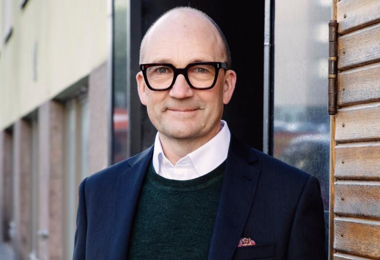 Kuvassa on Thomas de Mallet Burgess puolivartalokuvassa ja taustalla on vanha talo.