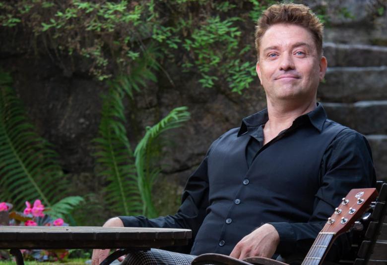 Kuvassa on Tuomas Lehto istumassa taustallaan viherkaskveja ja oikealla kiviportaat.