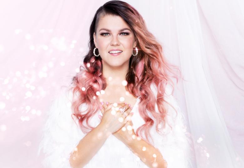 Kuvassa on Saara Aalto puolivartalokuvassa ja taustalla on valkoista verhoa ja Aallolla valkoinen puku sekä kädet ristikkäin rinnan päällä.