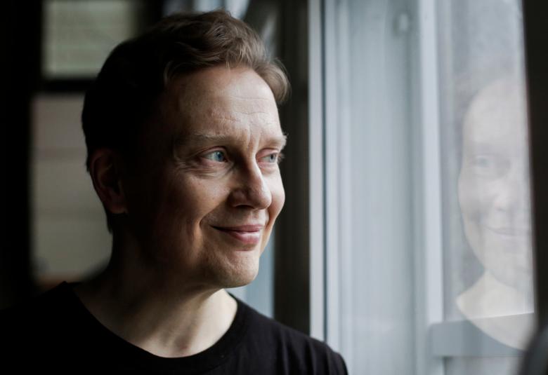 Kuvassa on Teemu Mäki, joka katsoo sivuun lasin läpi.  Lasista heijastuvat hänen kasvonsa.