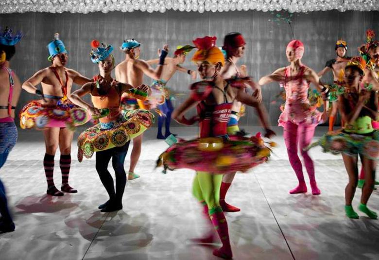 Kuvassa on balettitanssijoita värikkäissä ja erilaisissa asuissa, useimmat klassisen balettiasun tyyppisessä kirjavassa asussa lavalla tanssimassa.