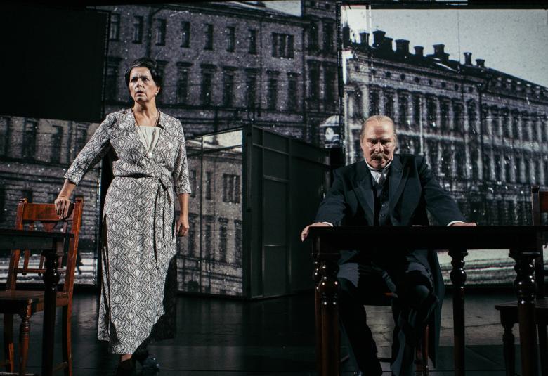 Kuvassa on taustalla presidentin linna ja etualalla vasemmalla on Kristiina Halttu Esterinä harmaa kuvioisessa puvussa seisomassa ja oikealla Vesa Vierikko istumassa.