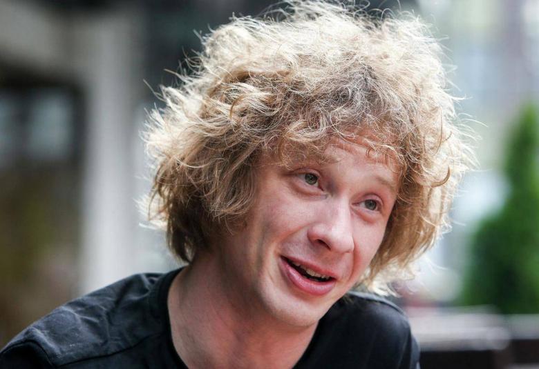 Kuvassa ovat Santtu-Matias Rouvalin kasvot ja katse on oikealle.  Hänellä on kiharaiset kasvot ja musta t-paita päällään.