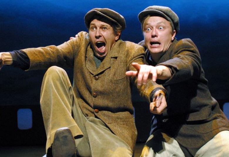 Kuvassa ovat Martti Suosalo ja Mika Nuojua ruskehtavissa vaatteissa ja käsiä ojennettuna eteenpäin osoittaen ja hiukan kauhistuneet ilmeet kasvoillaan.