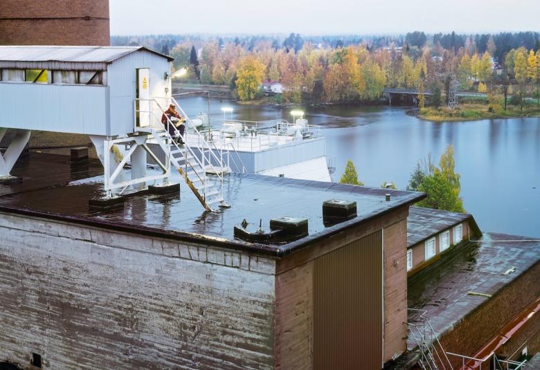 Kuvassa on proomu, jonka kannella on mies juomassa aamukahvia.  Proomu on valkoinen ja veden takana näkyy kaupungin silhuettia.