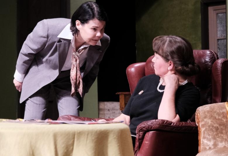 Kuvassa on kaksi naista, joista toinen on kumartuneena sohvalla istuvan puoleen.