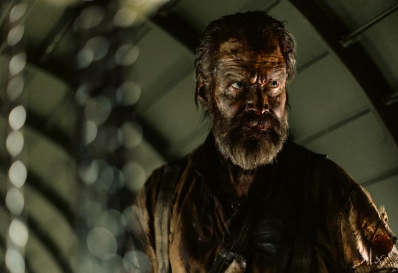 Kuvassa on Jorma Tommila päässään kypärämäinen päähine ja arta. Kuvan sävy on tumma.