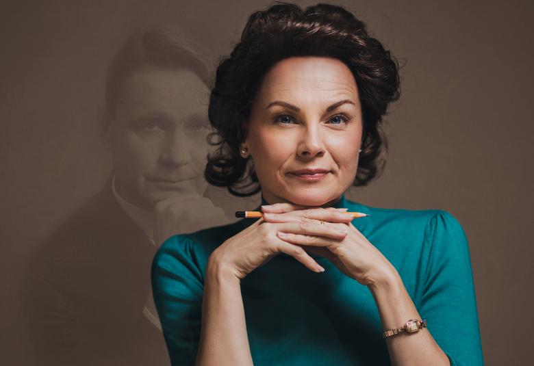 Kuvassa on Tellervoa esittävä näyttelijä ja kuvassa hän istuu pöydän ääressä kädet leuan alla ja hänellä on turkoosi kiiltävä pusero päällään. Taustalla on ruskeaa seinää, josta heijastuu Mauno Koiviston kasvot.