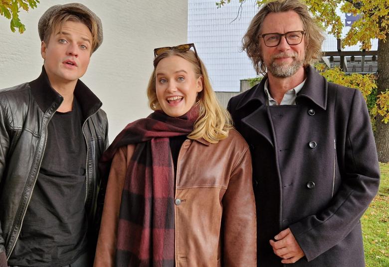 Kuvassa ovat Mikael Saari mustassa nahkatakissa, Aurora Manninen ruskeassa nahkatakissa ja Antti Reini mustassa takissa. Kuva on puolivartalokuva ja otettu ulkona.