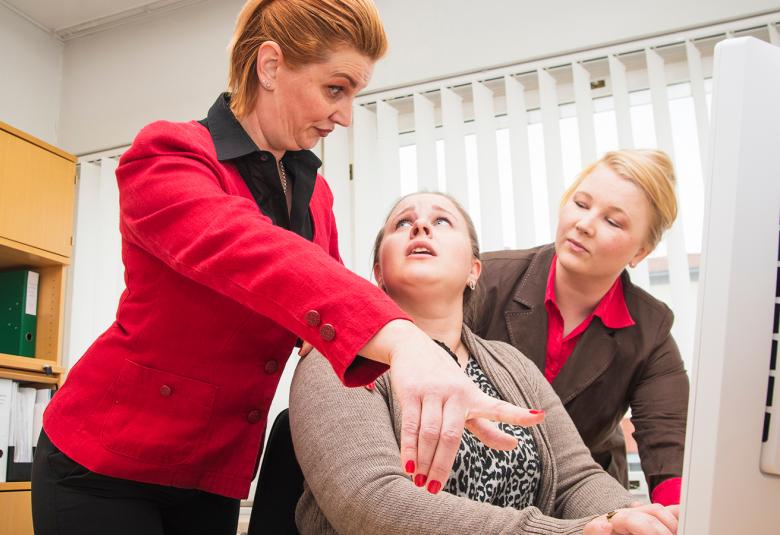 Kuvassa on kolme naista, joista yksi istuu toimistopöydän ääressä tietokoneella, keskustelevat.