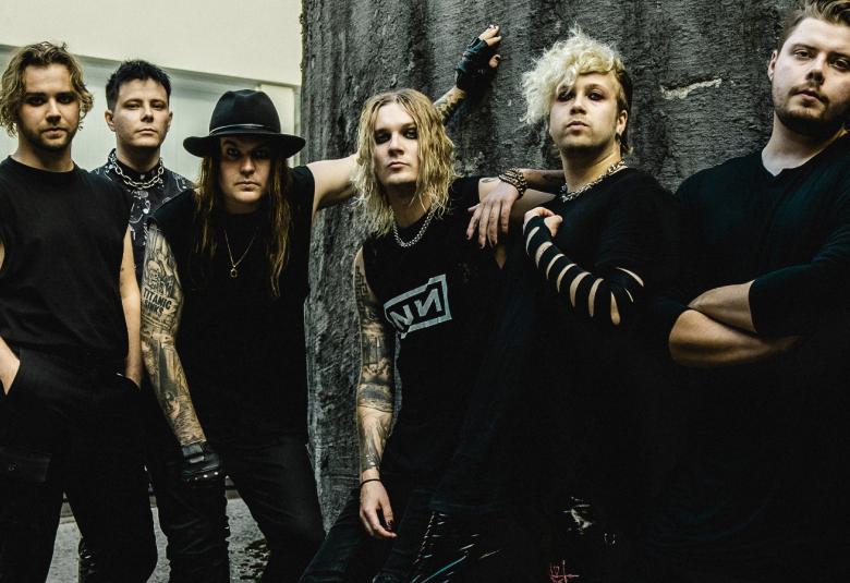 Kuvassa ovat Blind Channelin jäsenet mustissa t-paidoissa ja he ovat harmaan seinän vieressä.