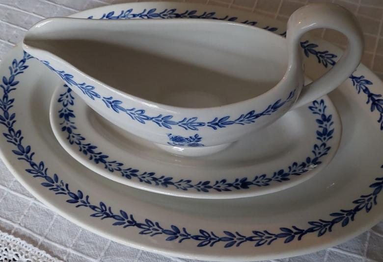 Kuvassa on soikeiden tarjoilulautasten päällä kastikekulho, jossa on reinassa sinisiä kuvioita kuten lautasissakin.