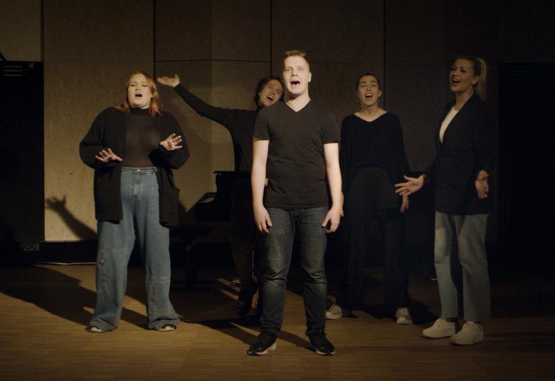 Kuvassa ovat Hoosiannan viisi laulajaa tummahkossa kuvassa ja yksi heistä on keskellä kuvaa.