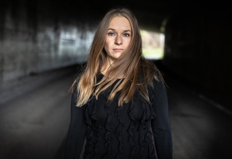 Kuvassa on Satu Rämö seisomassa kaartuvassa tunnelissa. Kuva on otettu pimeällä.