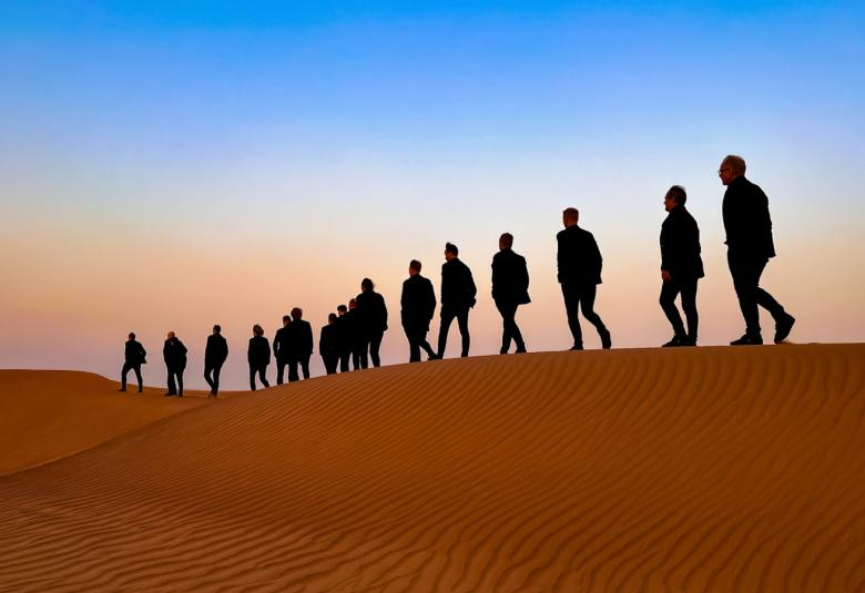 Kuvassa ovat Semmarit aaltoilevan hiekkadyynin päällä ja he ovat pienevässä järjestyksessä.  Taustalla on sininen taivas.