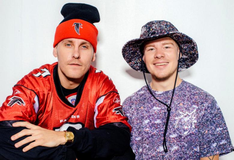 Kuvassa ovat artistit Jare ja VilleGalle.  Jarella on puna-musta pipo päässään ja VilleGallella sininen lierihattu.