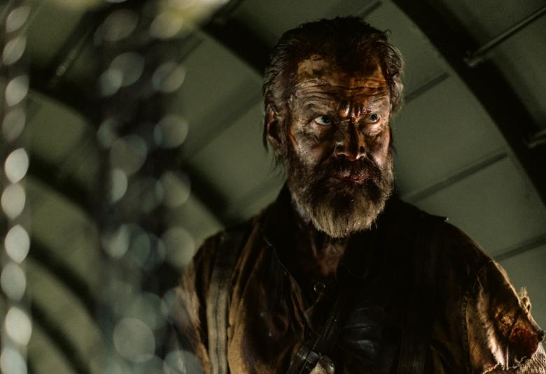 Kuvassa on Jorma Tommila hämärässä tilassa. Tommila on parrakas ja hänellä on tumma paita päällään.