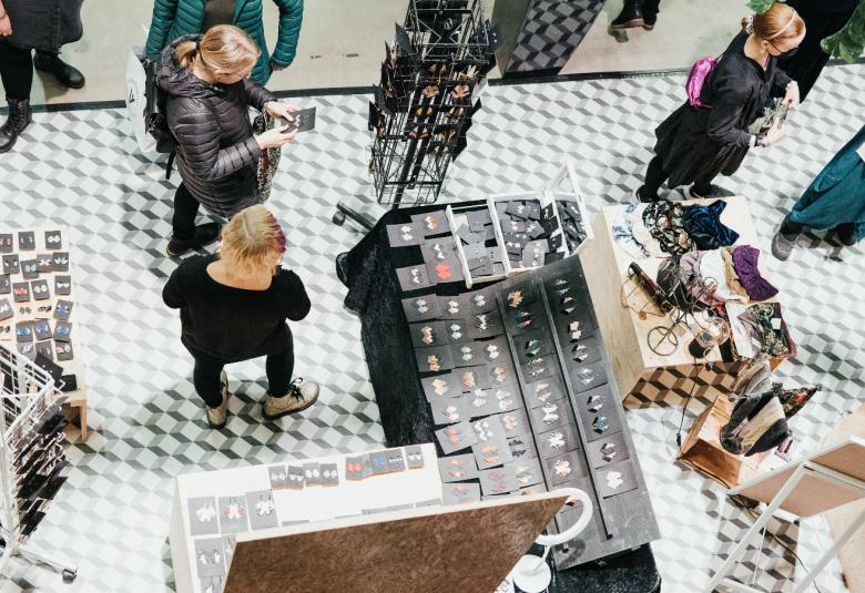 Kuvassa on ylhäältä päin otettuna myyntipöytiä ja niiden keskellä käveleviä messukävijöitä.