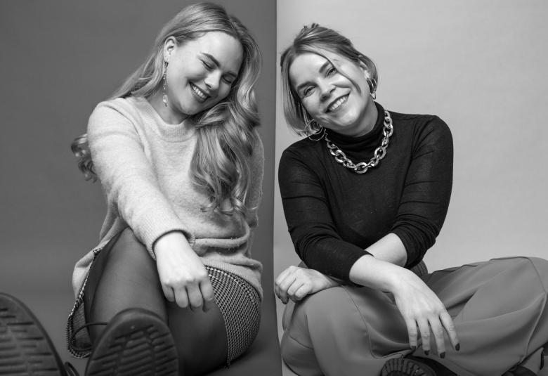Kuvassa ovat vasemmalla Laura Wathén ja oikealla Katri Ylinen eri kuvissa istumassa lattialla iloisilla ilmeillä. Kuva on musta-valkoinen.