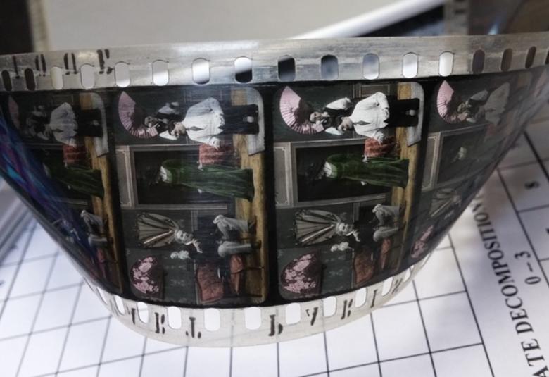 Kuvassa on vanhanaikaista filmiä pöydällä ja laajasti kiertyneenä nauhana. Pohjana on valmoisella pohjalla ruudukkoa.