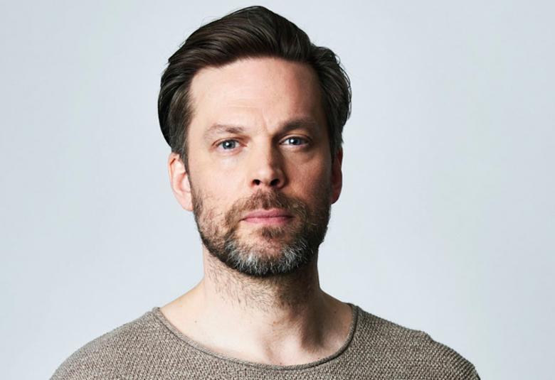 Kuvassa on Mikko Nousiainen kasvokuvassa.  Hänellä on hieman partaa ja päällään ruskeä t-paita.