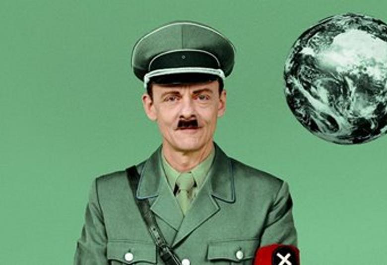 Kuvassa on Olaf Johannessen harmaassa asepuvussa Diktaattorina.  Tausta on vihreä.