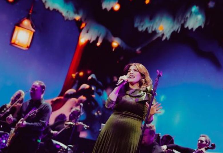 Kuvassa on Suvi Teräsniska mustassa mekossa lavalla ja kuva on otettu vinosti. Taustalla on bändi ja sinistä valoa.