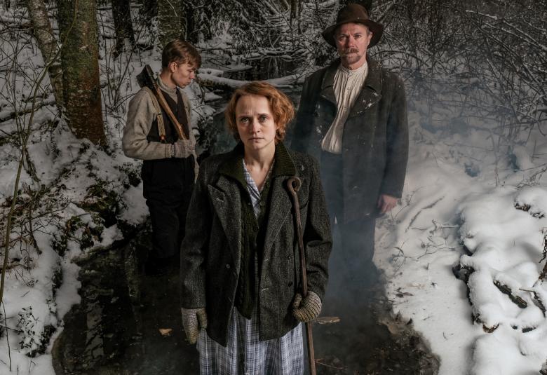 Kuvassa on vasemmalla sivuttain Verneri Lilja ja edessä Ella Määttänen.  Takana on Esa Latva-Äijö taustallaan maisema, jossa on jonkin verran lunta ja keskellä on virta. Henkilöillä on työvaatteet päällä ja he seisovat virrassa.