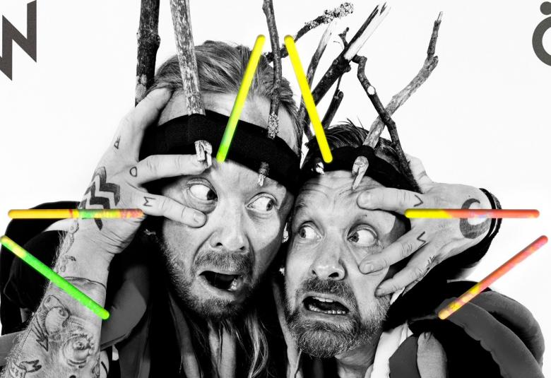 Kuvassa ovat Antti ja Jussi Hyyrynen, jotka vääntelevät kasvojaan sekä pitelevät kasvojaan.  Kuvassa on keltaisia ja msutia tikkuja siellä täällä kuvaa.  Vasemmalla on musta kaksois-V-kirjain ja oikealla -kirjain.