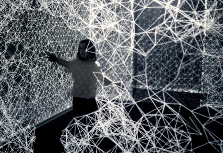 Kuvassa on mustalla taustalla valkoista verkkoa ja sen keskellä on tyttö katselemassa verkkoja.  Kuva On musta-valkoinen.