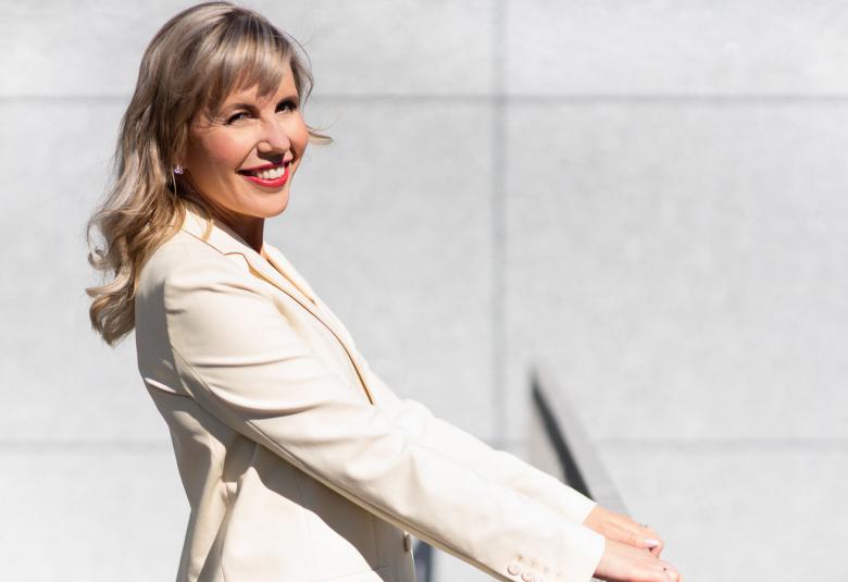 Kuvassa on Kaisa Rönkkö puoliksi sivuttain valkoisessa jakussa puolivartalokuvassa.